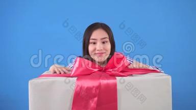 积极向上的年轻亚洲女人从蓝色背景上的一个巨大的<strong>礼</strong>品盒中看出来